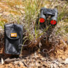 Black binoculars resting on shrub in bushland next to black protective case